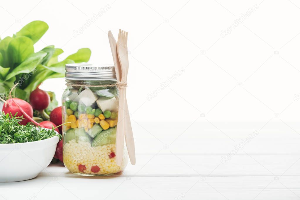 fresh vegetable salad in glass jar near radish isolated on white