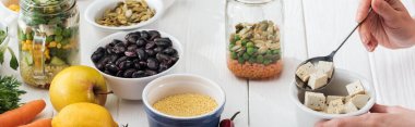 ahşap beyaz masa, panoramik çekim üzerinde cam kavanozda tofu peyniri ekleyerek kadın kırpılmış görünümü