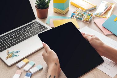 elinde dijital tablet tutan kadın kırpılmış görünümü, saksı, kırtasiye ve dizüstü çiçek ile ahşap masa arkasında oturan