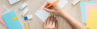 cropped view of woman writing notes at to do list, sitting behind wooden table with stationery clipart