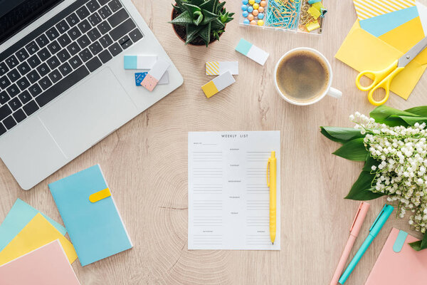 верхний вид еженедельного списка, канцелярские принадлежности, чашка кофе и ноутбук на деревянном столе
