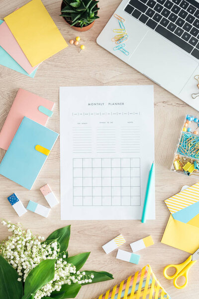 top view of monthly planner, stationery, flowers and laptop on wooden table