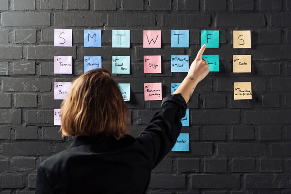 back view of woman pointing with finger at colorful sticker notes on black brick wall