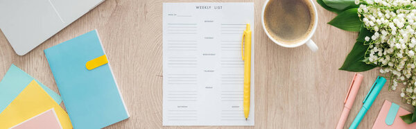 panoramic view of weekly list, flowers, laptop and coffee cup on wooden table