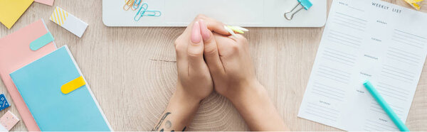 cropped view of woman holding hands on wooden table with weekly list and stationery