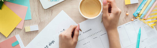 cropped view of woman with cup of coffee holding hands on planners and check lists