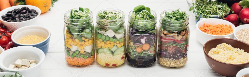 fresh vegetable salad in glass jars on wooden white table isolated on white, panoramic shot