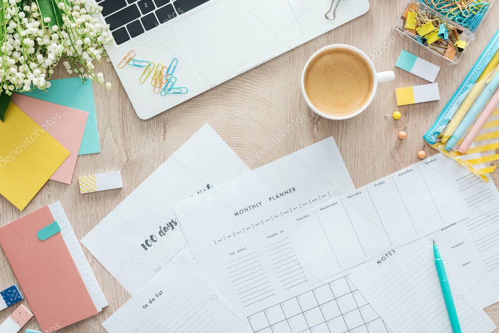 top view of planners, stationery, cup of coffee and laptop on wooden table