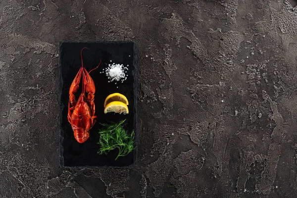 在灰色纹理表面上与红龙虾 柠檬片和绿色香草的黑盘的顶视图 — 图库照片