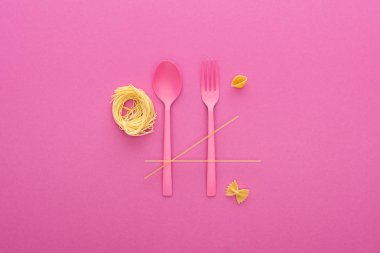 pink plastic spoon and fork near different kinds of pasta isolated on pink clipart
