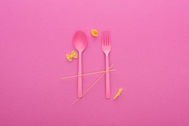 pink plastic spoon and fork and four different kinds of pasta isolated on pink clipart