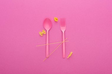 pink plastic spoon and fork and four different kinds of pasta isolated on pink clipart