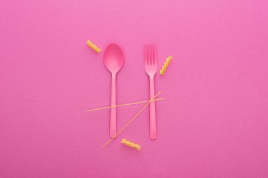 pink plastic spoon and fork and two different kinds of pasta isolated on pink clipart