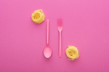 pembe arka planda erişte makarna yakınında baş aşağı pembe plastik çatal ve kaşık