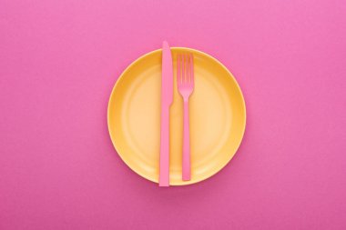 top view of pink plastic fork and knife on yellow plastic plate on pink background clipart