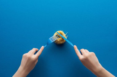 mavi plastik çatal tutan ve mavi arka plan üzerinde bıçak ile erişte makarna kesme kadın kırpılmış görünümü