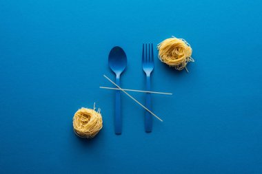 mavi arka planda erişte makarna yakın spagetti ile mavi plastik kaşık ve çatal üst görünümü