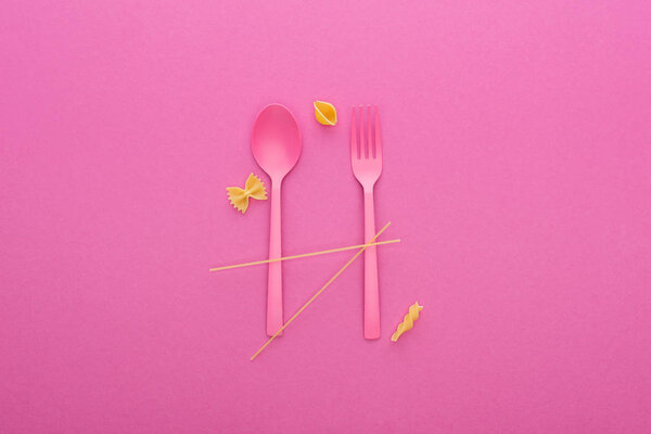 pink plastic spoon and fork and four different kinds of pasta isolated on pink