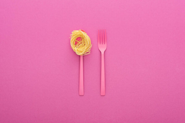 pink plastic fork and pasta on pink spoon on pink background