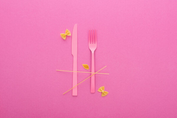 pink plastic knife and fork, spaghetti, uncooked farfalle pasta and shell macaroni isolated on pink