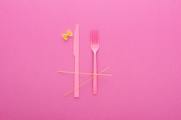 pink plastic knife and fork, spaghetti and uncooked farfalle pasta isolated on pink