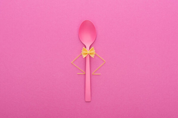 uncooked farfalle pasta on plastic spoon and spaghetti isolated on pink