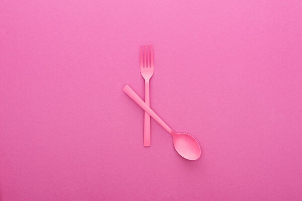 crossed pink plastic fork and spoon isolated on pink