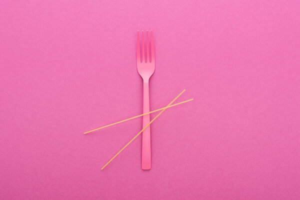 top view of pink plastic fork and spaghetti isolated on pink