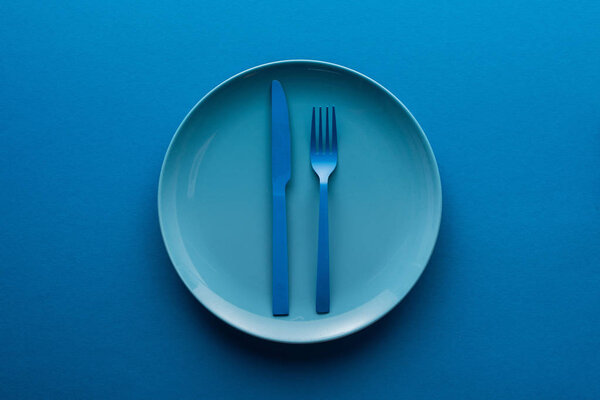 blue plastic knife and fork on plate on blue background