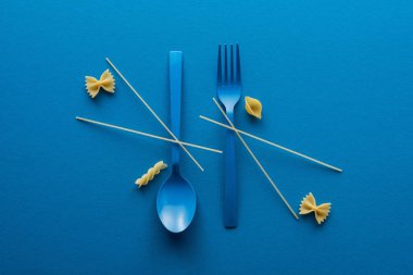mavi arka plan üzerinde pişmemiş makarna farklı türde yakın mavi plastik kaşık üzerinde spagetti düz yatıyordu ve çatal