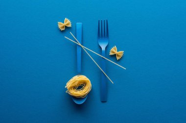 mavi arka planda farfalle makarna yakın çatal ve kaşık üzerinde spagetti ile mavi plastik kaşık üzerinde erişte makarna