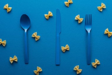 mavi arka plan etrafında pişmemiş farfalle makarna ile mavi plastik çatal