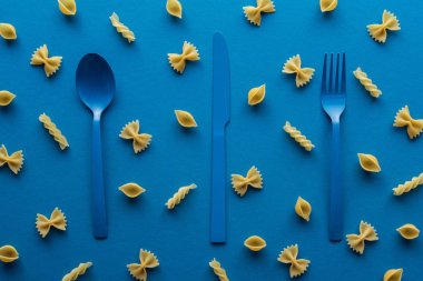 mavi arka plan etrafında pişmemiş makarna ile mavi plastik çatal