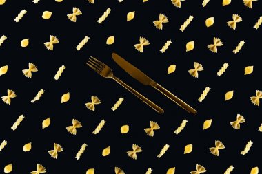 flat lay of different kinds of pasta with metal cutlery in middle isolated on black clipart