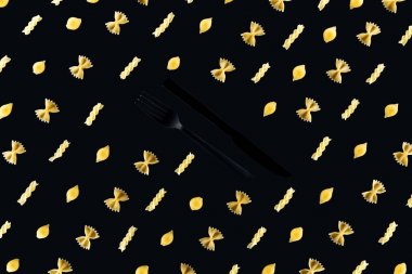 flat lay of different kinds of pasta with plastic black fork and knife in middle isolated on black clipart