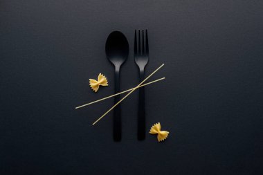 siyah arka plan üzerinde farfalle makarna ve spagetti ile plastik kaşık ve çatal