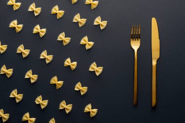 siyah arka plan üzerinde altın bıçak ve çatal yakın farfalle makarna düz yatıyordu
