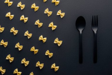 siyah arka plan üzerinde plastik kaşık ve çatal yakın farfalle makarna düz yatıyordu