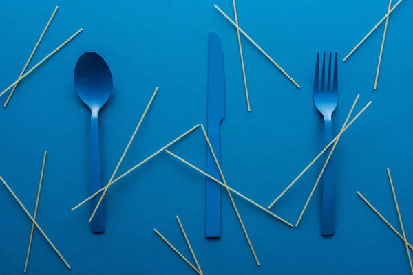 Blå Plastbestick Med Okokt Spaghetti Runt Blå Bakgrund — Stockfoto