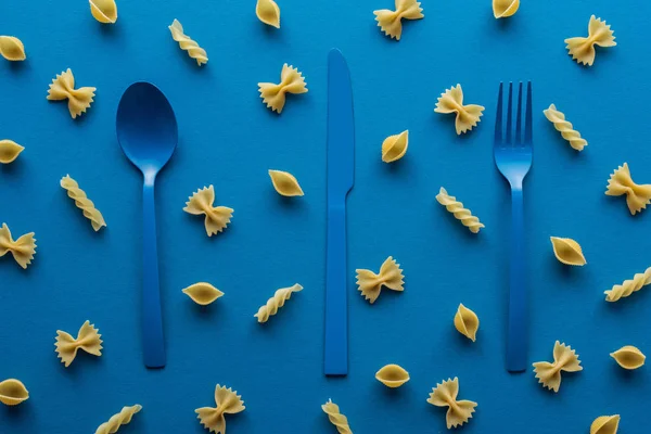 Blauwe Kunststof Bestek Met Ongekookte Pasta Rond Blauwe Achtergrond — Stockfoto