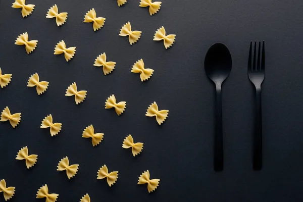 Flat Lay Farfalle Pasta Nära Plastsked Och Gaffel Svart Bakgrund — Stockfoto