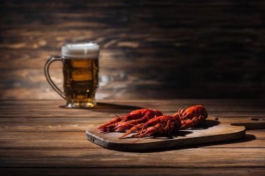 selective focus of red lobsters and glass with beer on wooden surface clipart