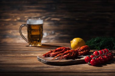 ahşap yüzeyüzerinde bira ile kırmızı ıstakoz, domates, dereotu, limon ve cam