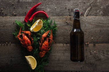 top view of red lobsters, lemon slices, dill, pepper and bottle with beer on wooden surface clipart