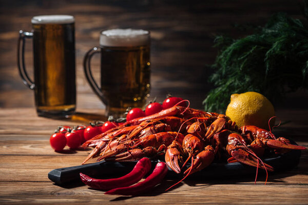 selective focus of red lobsters, tomatoes, dill, lemon and glasses with beer on wooden surface