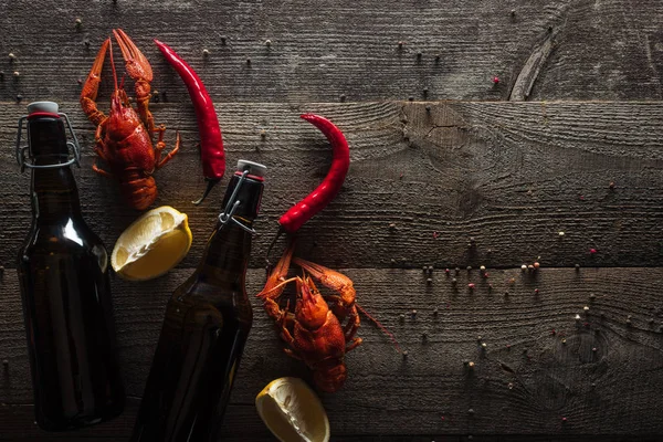 stock image top view of red lobsters, lemon slices, pepper and bottles with beer on wooden surface