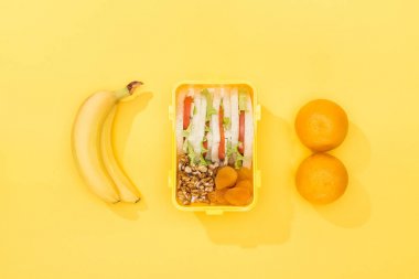 top view of nuts, dried apricots with sandwiches in lunch box near bananas and oranges clipart