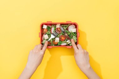 çatal ve bıçak tutan, öğle yemeği kutusundan salata yiyen kadın kırpılmış görünümü