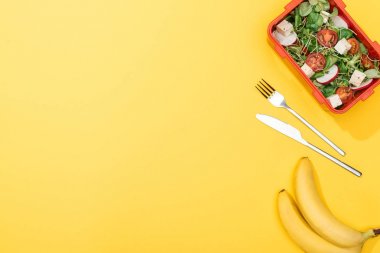 salata ile öğle yemeği kutusunun yanında muz, çatal ve bıçak üst görünümü