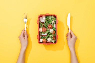 cropped view of woman holding fork and knife over lunch box with salad clipart